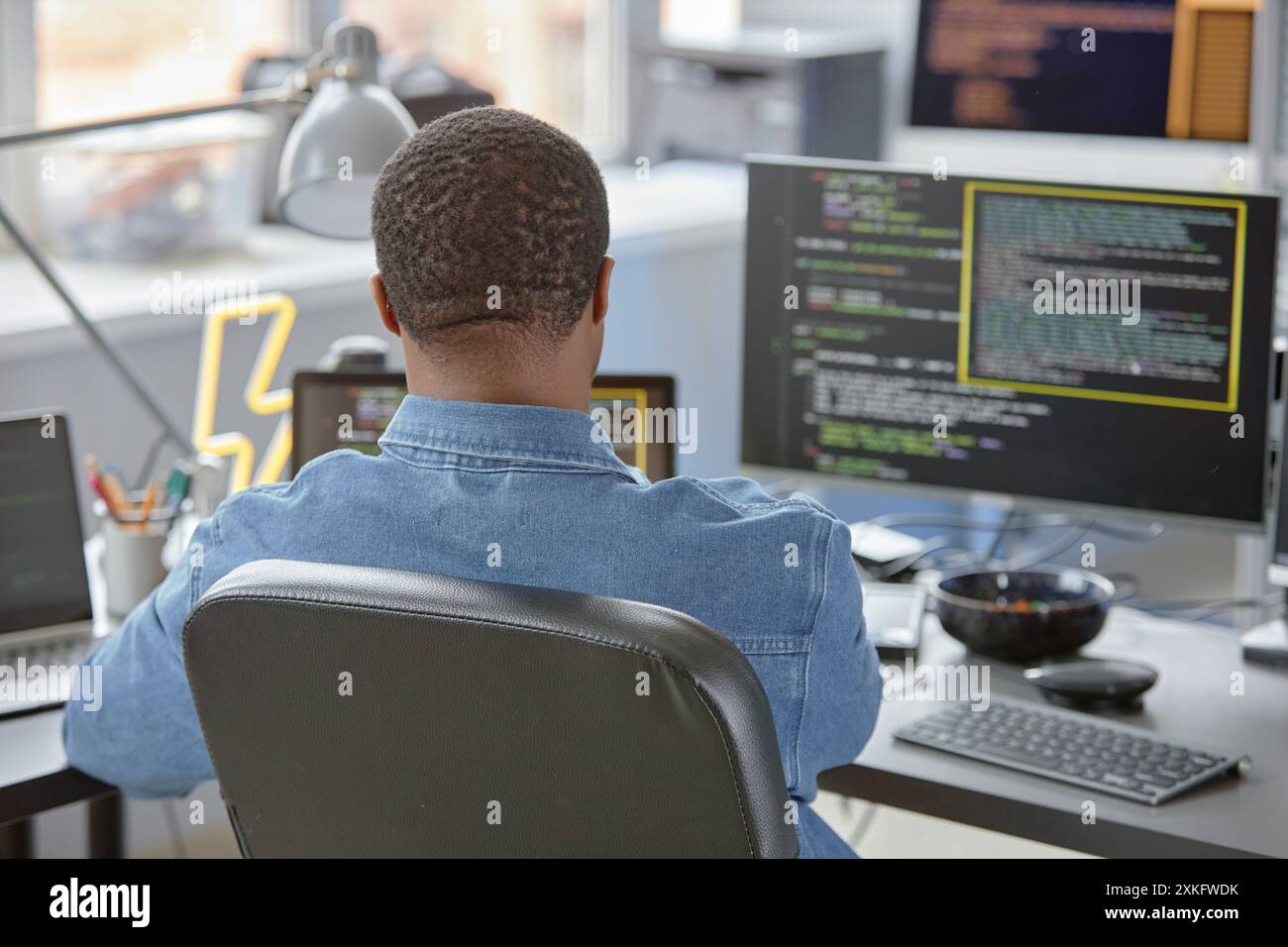 Rear view of male African American software engineer using computer at office desk for writing program code and finding errors Stock Photo