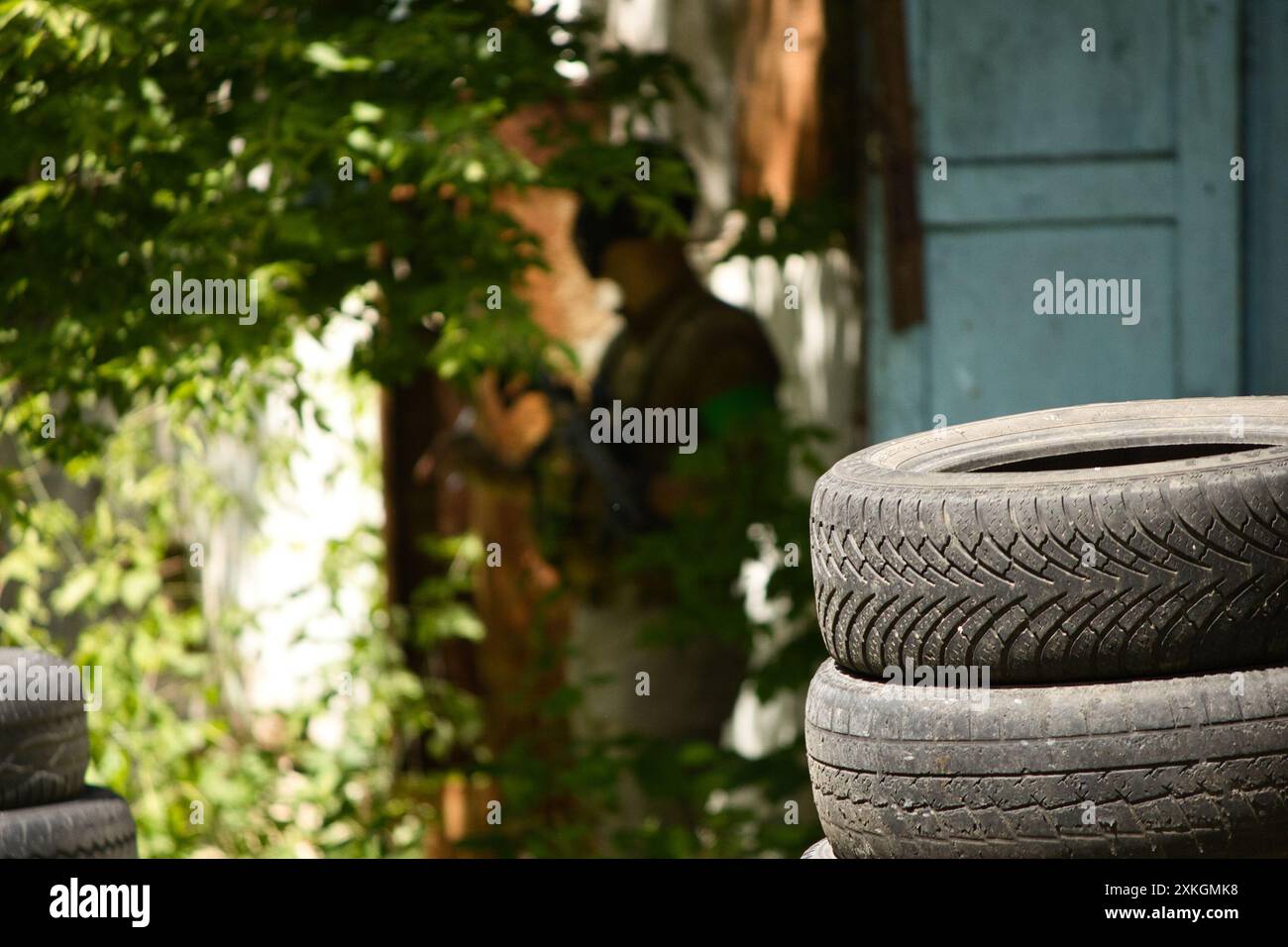 silhouette of a man with a gun near an old abandoned building, old tires everywhere Stock Photo