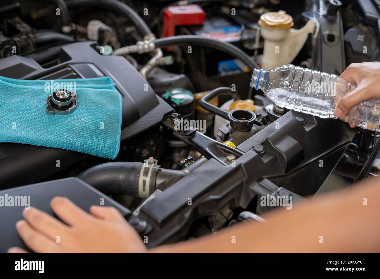 A young woman is filling the car's radiator with water, conducting a ...