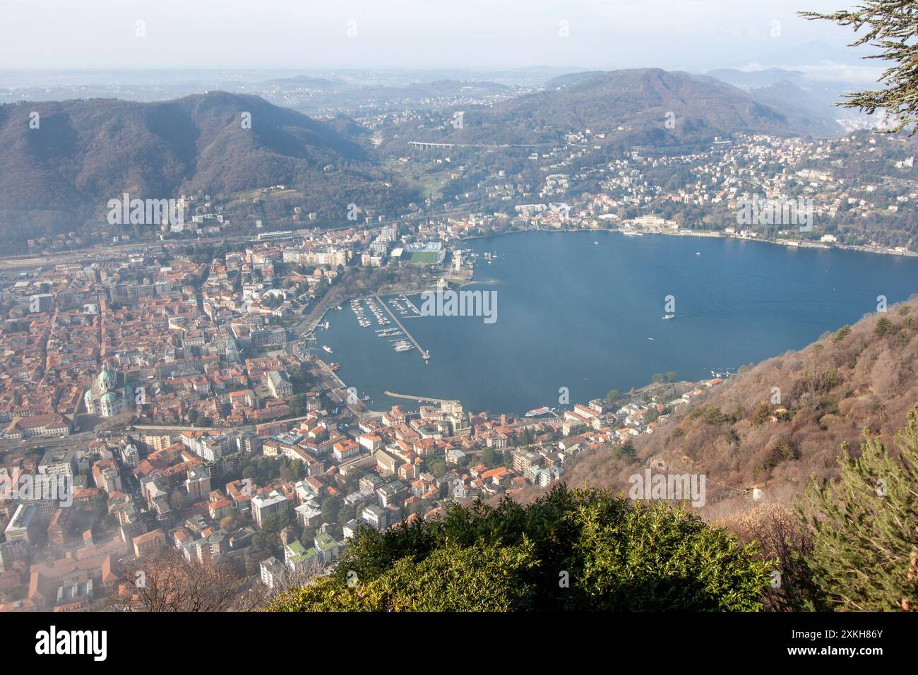 Panoramic view of Como city and the southern part of Lake Como from Brunate, showing the historic buildings, the deep blue lake, and surrounding mountains.