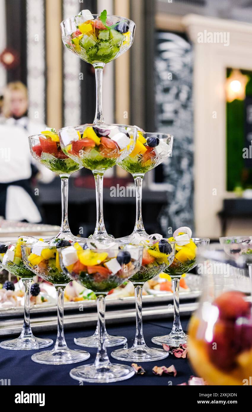 Close-up of elegant glassware filled with a colorful vegetable salad, arranged in a tiered presentation on a table. Vertical photo. Stock Photo