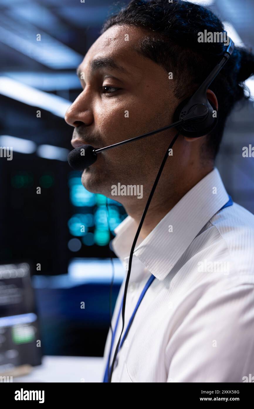 Data center agent supporting engineering team doing hardware maintenance, talking in headset microphone. Worker in high tech server room facility coordinating technicians using mic Stock Photo