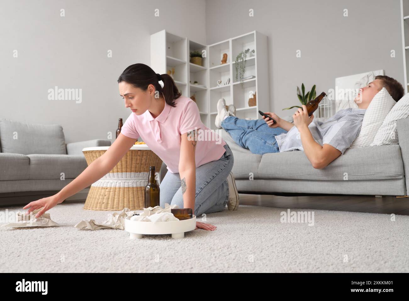 Stressed wife cleaning trash while her lazy husband with beer watching ...