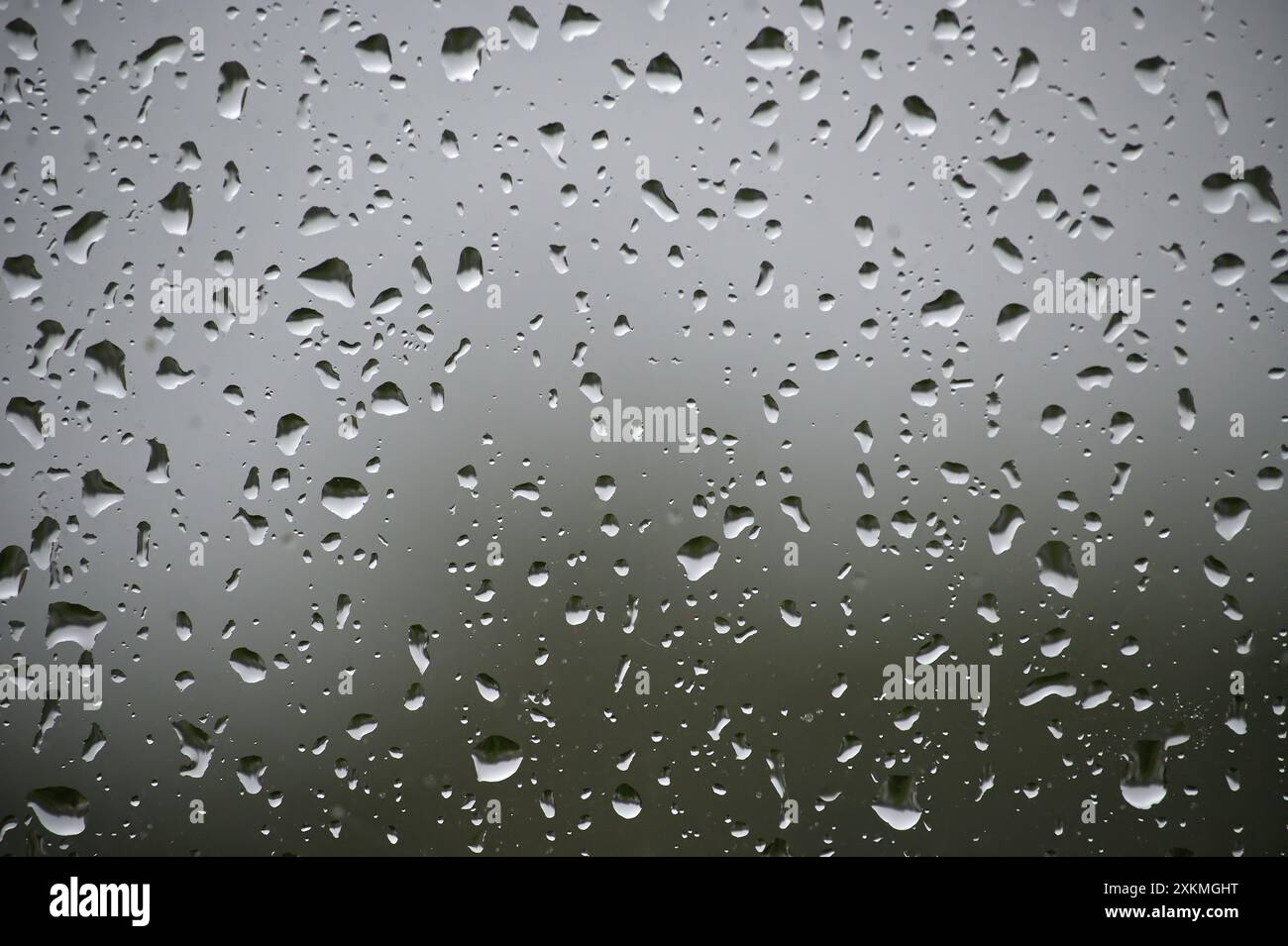 A window with raindrops on it. The raindrops are scattered all over the window, creating a blurry and hazy effect. Scene is calm and peaceful, as the Stock Photo