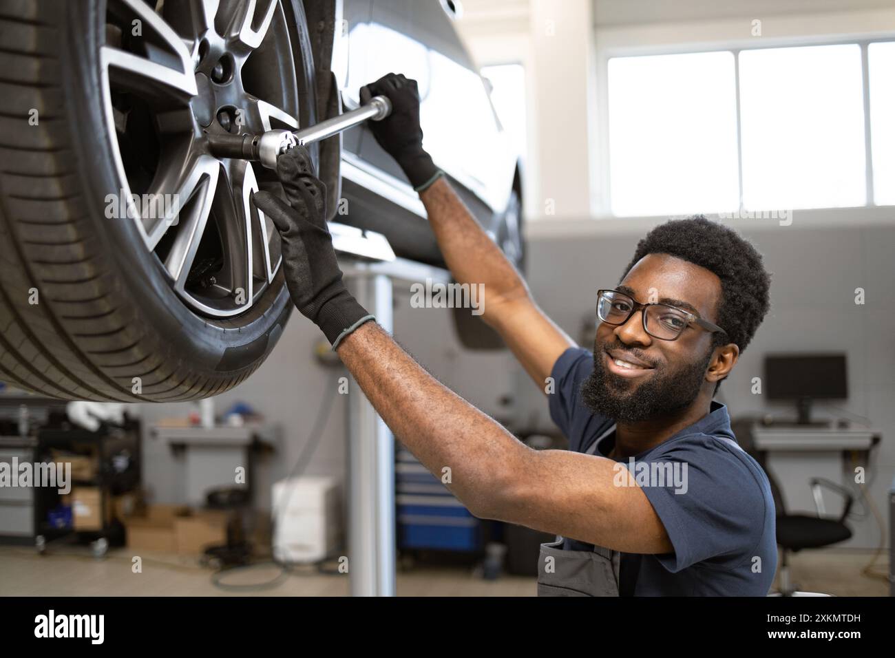 Smiling mechanic repairing car wheel in modern garage Stock Photo - Alamy