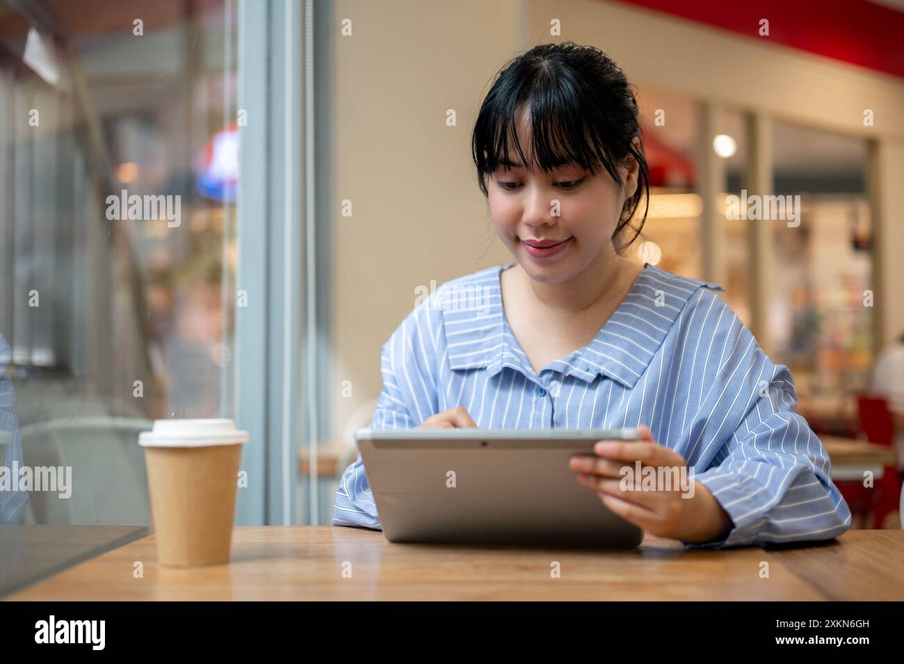 A charming young Asian woman using her digital tablet at a table in a ...
