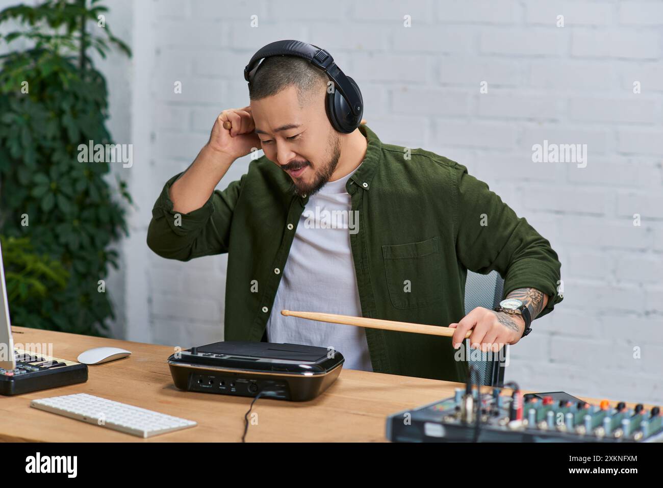 A young Asian man wearing headphones plays a drum pad in a recording studio. Stock Photo