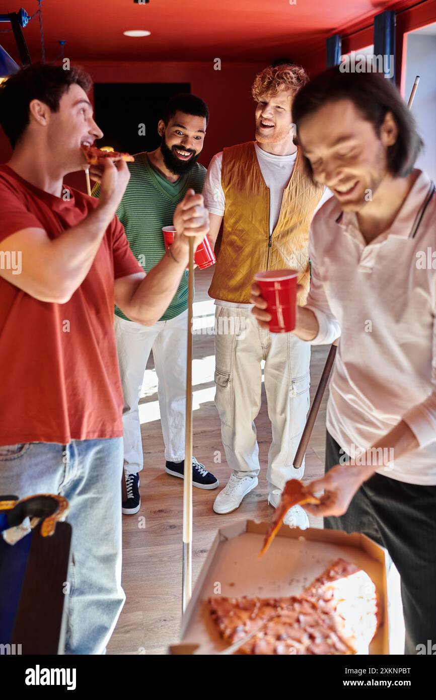 Friends gathered around a pool table, enjoying pizza and drinks. Stock Photo