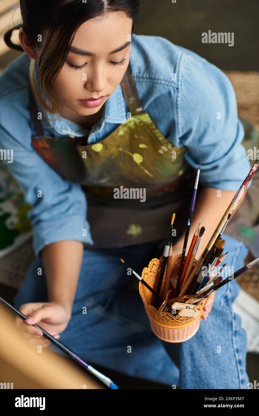 A young Asian woman artist is painting in her workshop, focusing ...