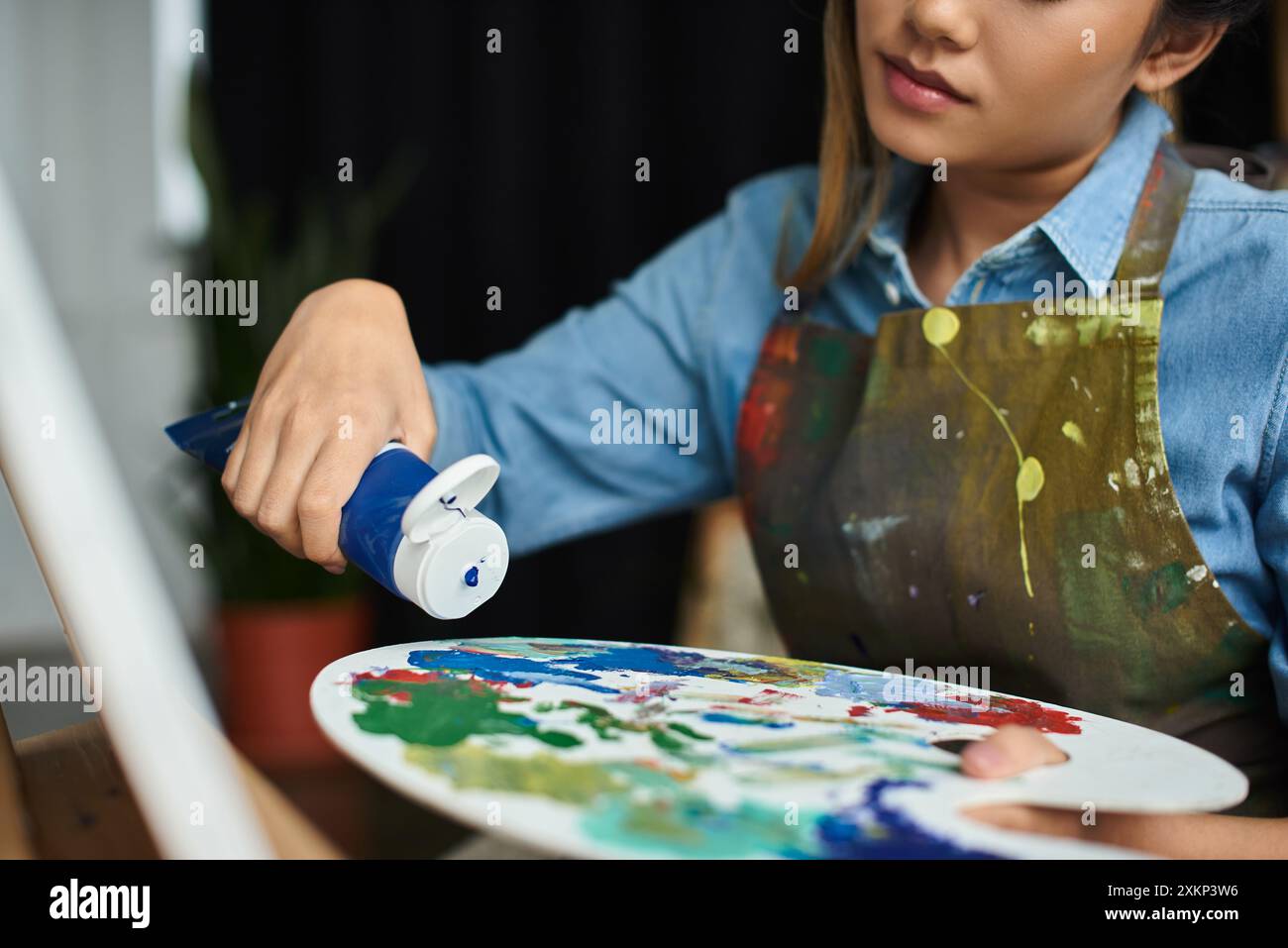 A young Asian woman in an apron squeezes paint from a tube into a ...