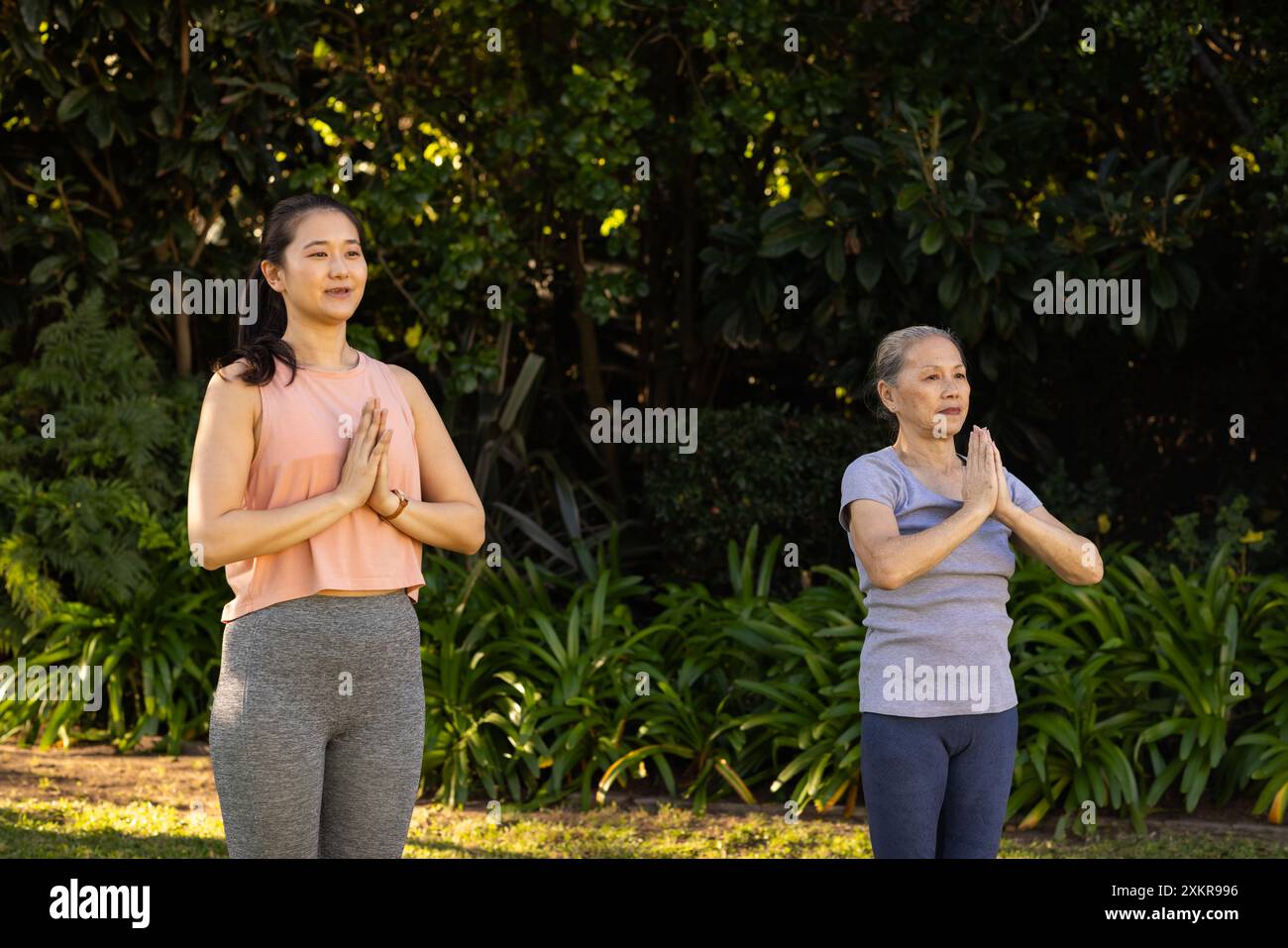 Practicing yoga, asian grandmother and granddaughter standing in prayer ...
