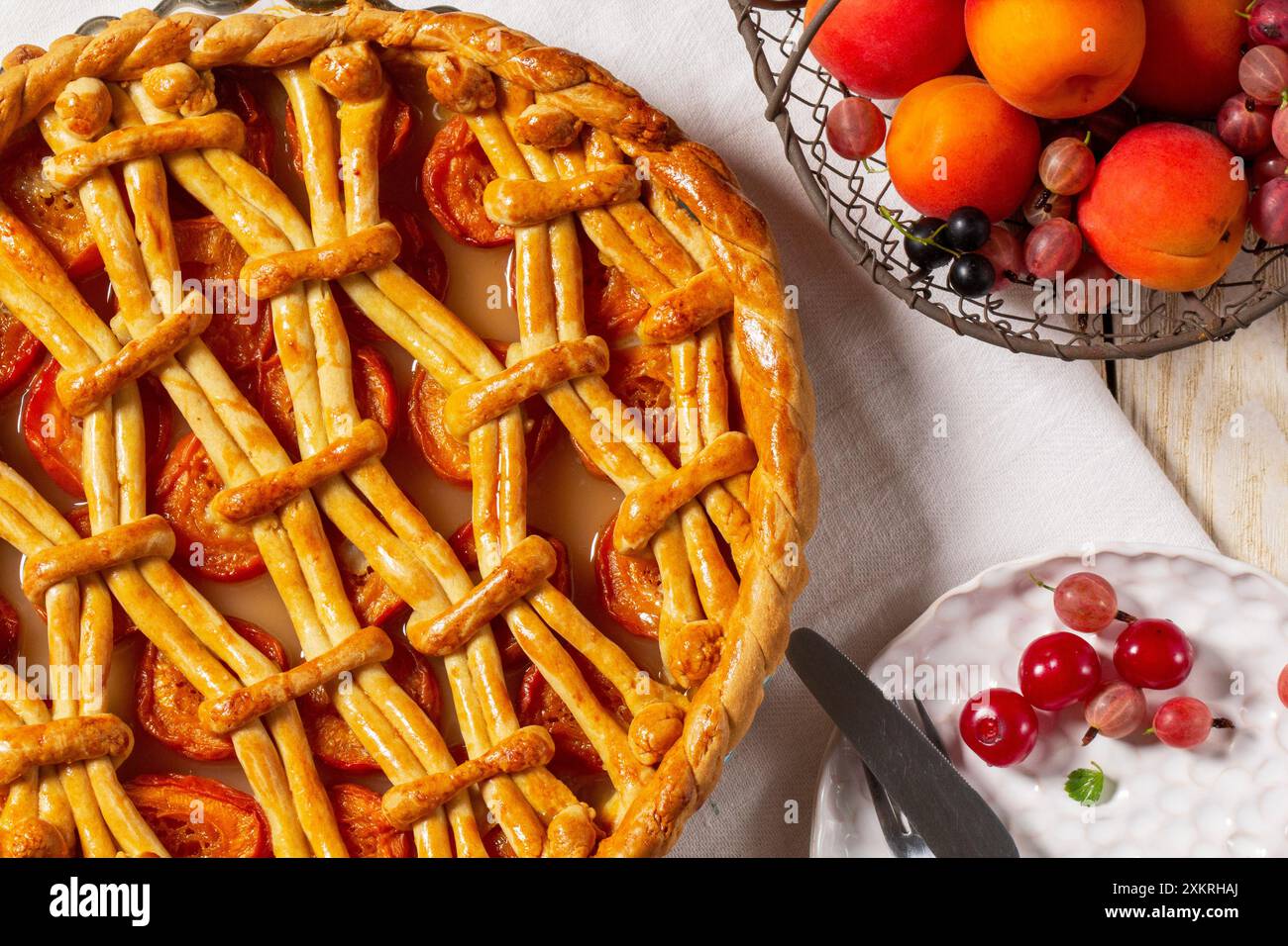 Apricot pie decorated with dough ornament and a metal basket with fruits and berries on a light background. Rustic style, selective focus. Stock Photo