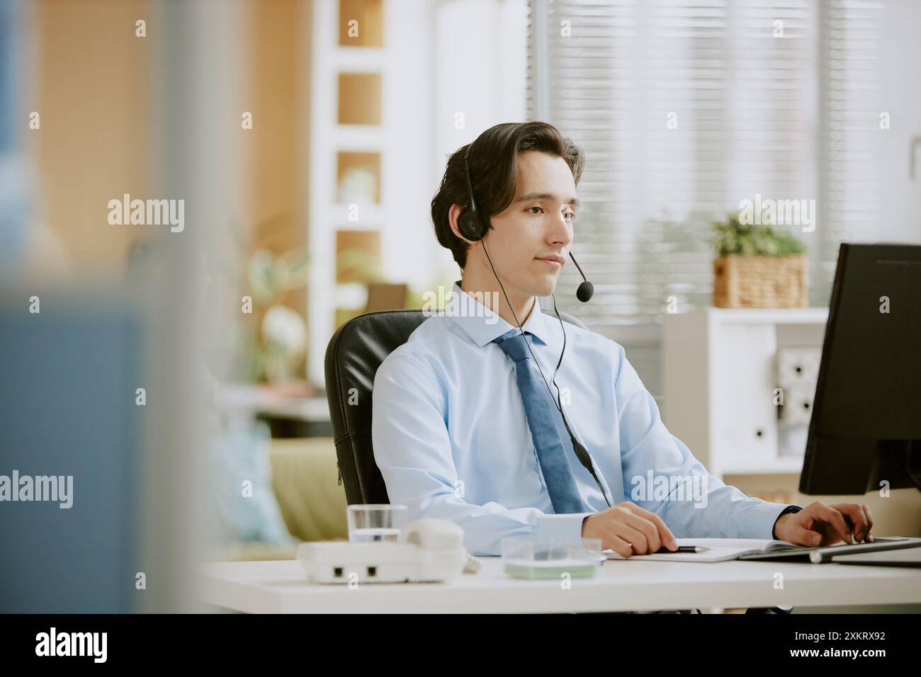 Young Caucasian call center male intern focused on work while using computer to write report Stock Photo