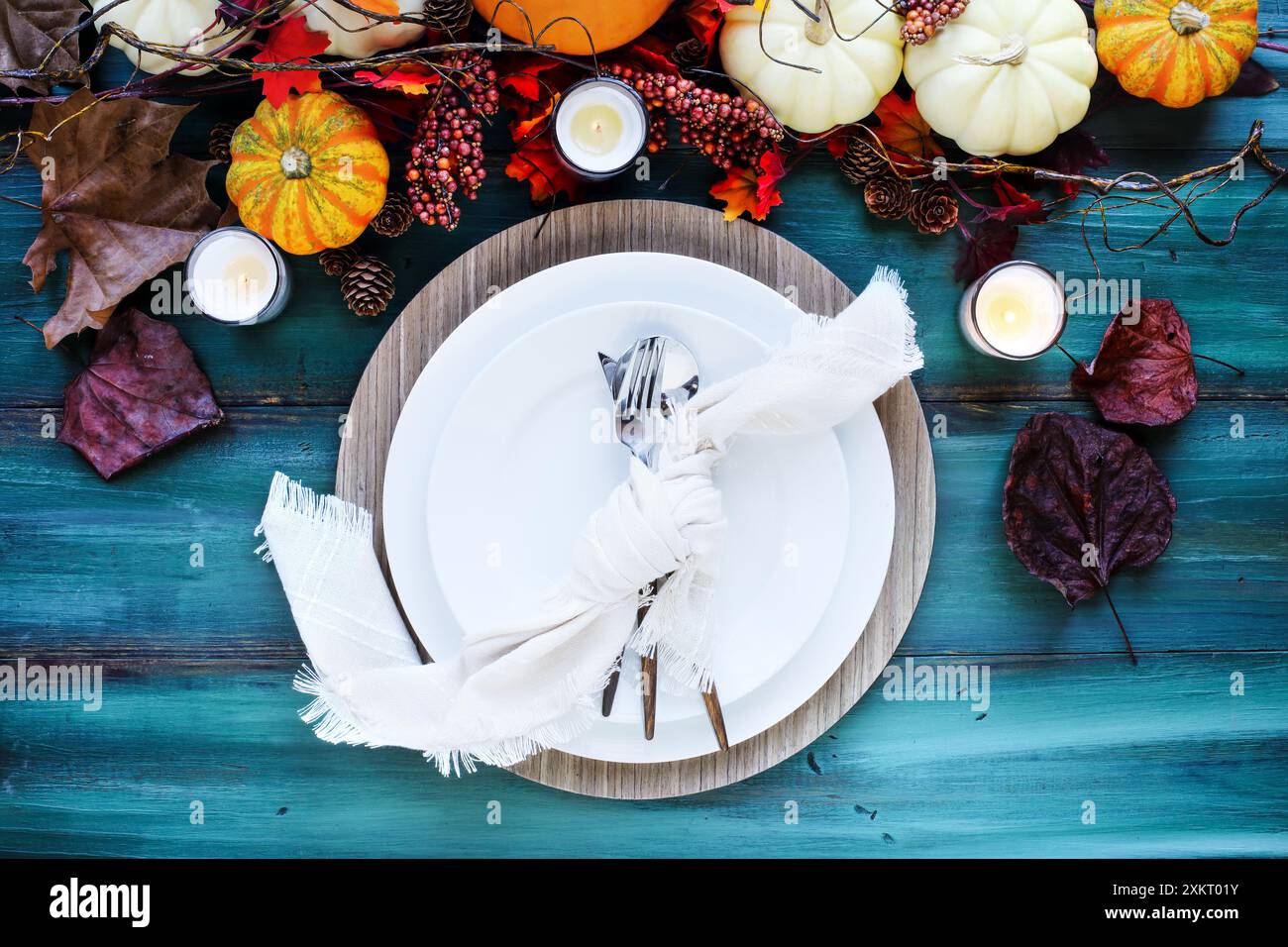 Flat lay of a white plates with napkin tied into a knot and silverware place setting over a rustic wood table with autumn garland. Stock Photo