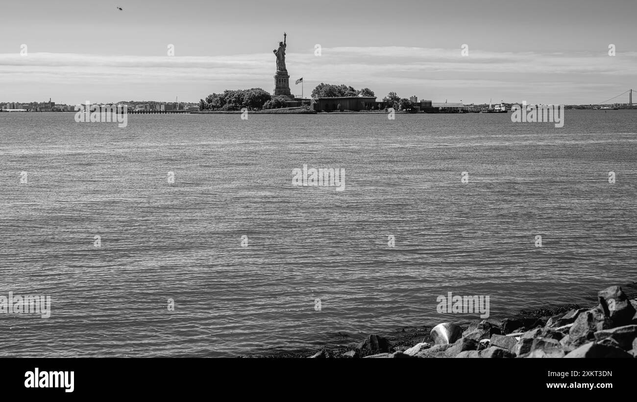 Captured from Liberty State Park, the Statue of Liberty stands tall as a helicopter circles Liberty Island. The American flag flies proudly, while a t Stock Photo