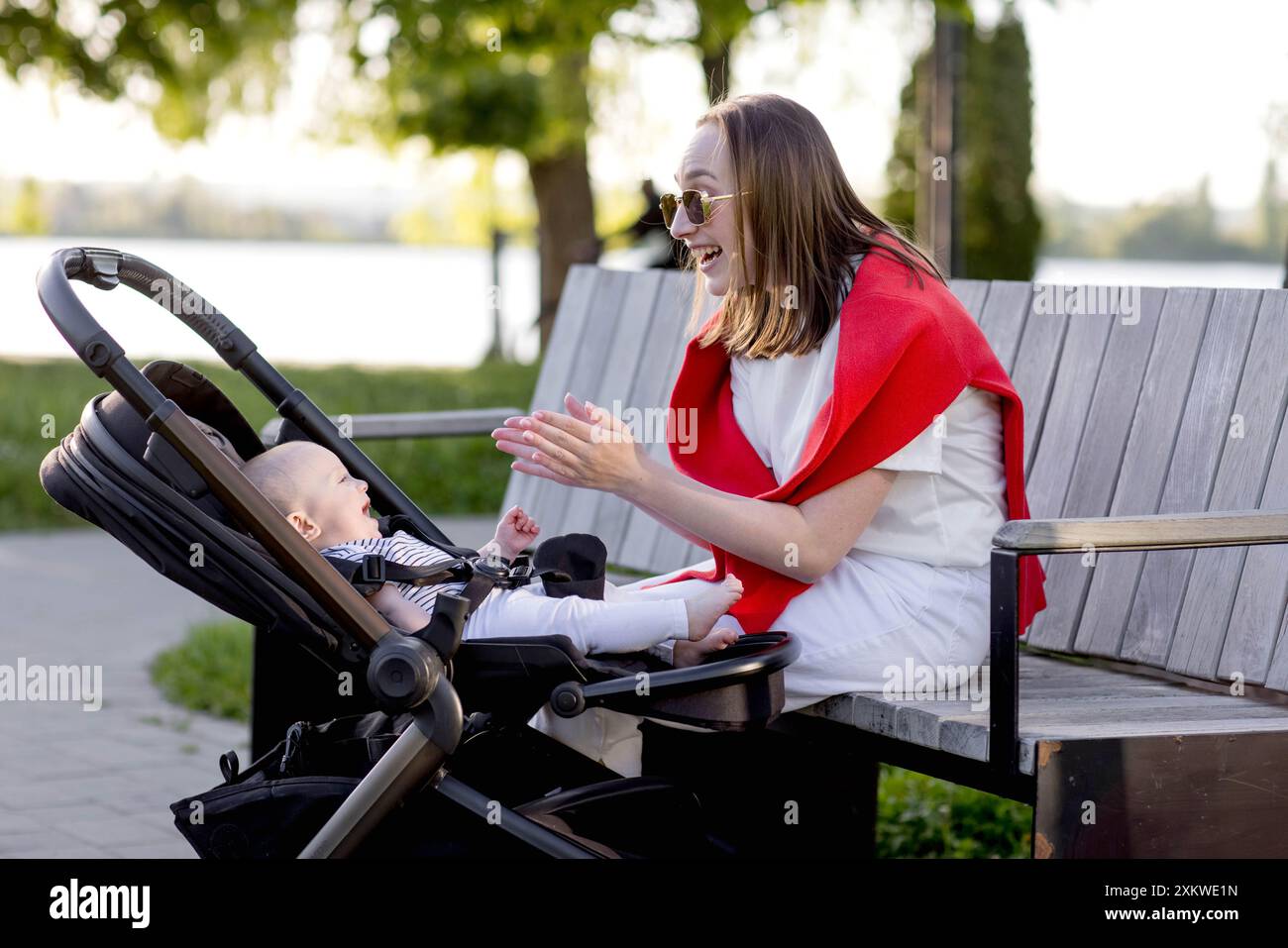 Young mother with her cute baby is sitting on a park bench Stock Photo ...