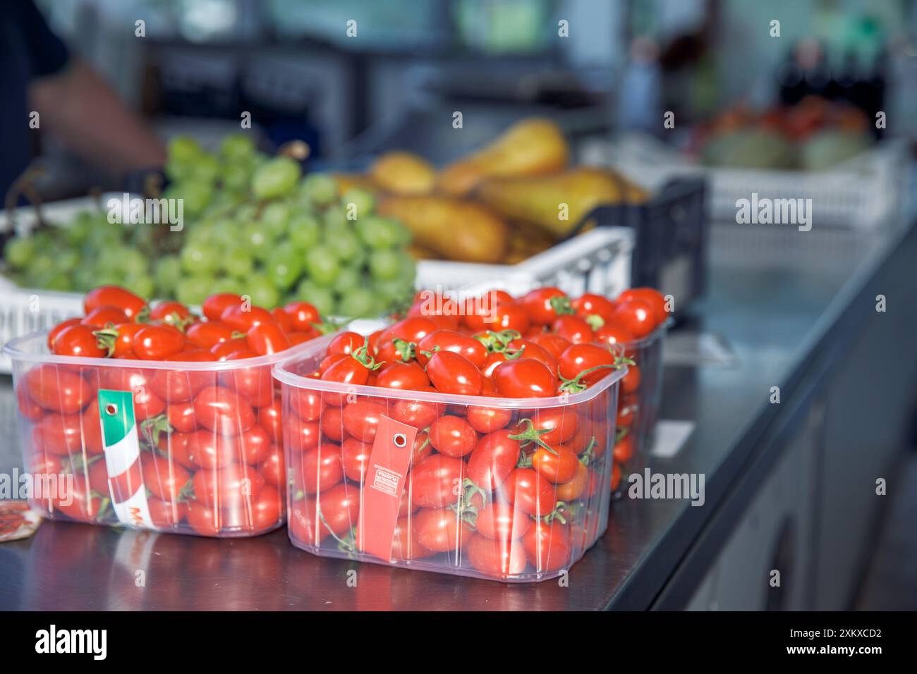 Plastic containers of fresh tomatoes on a market stall with various ...