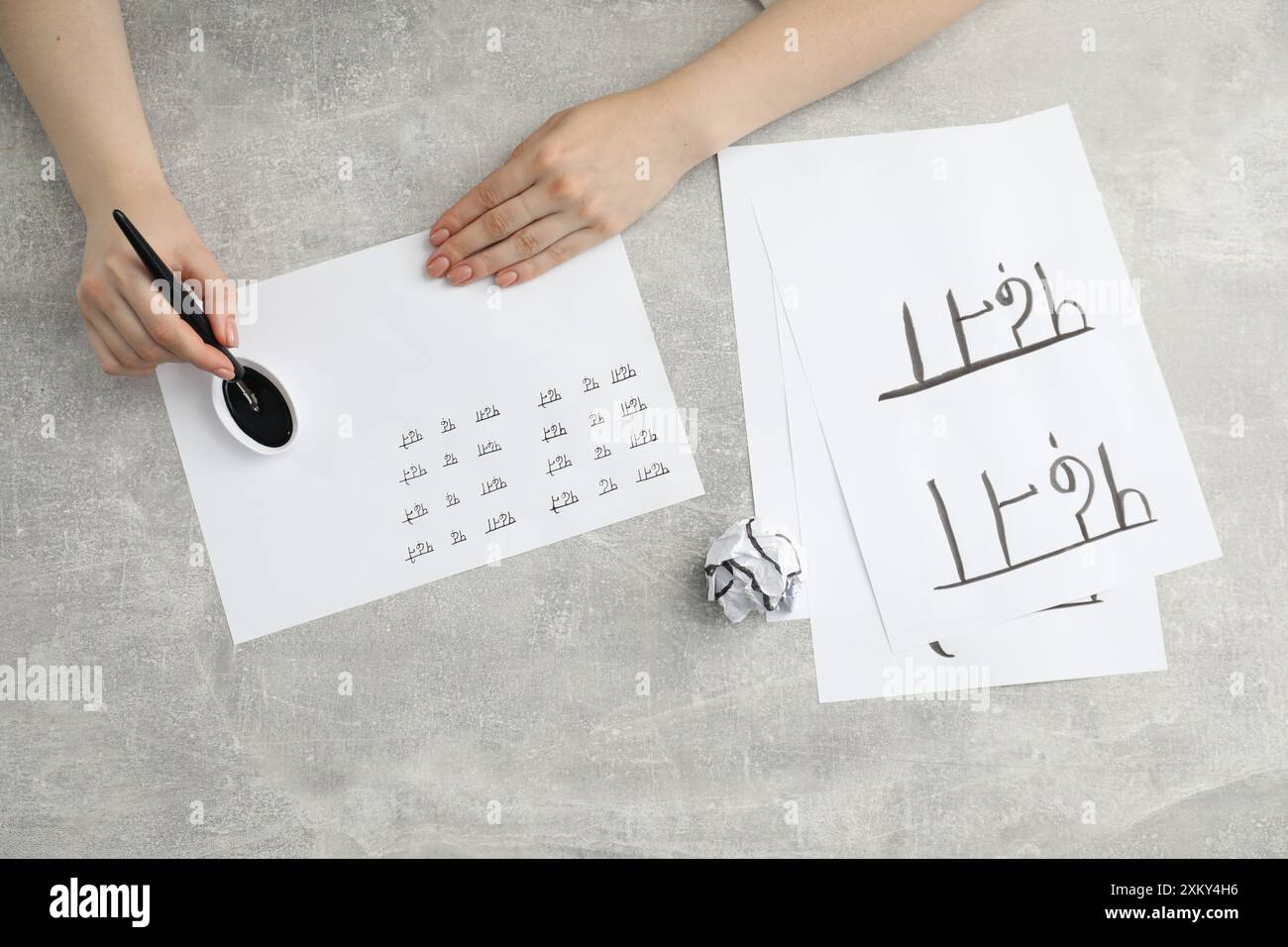 Calligraphy. Woman with fountain pen writing words Reading and Read in Hindi on paper at grey table, top view Stock Photo