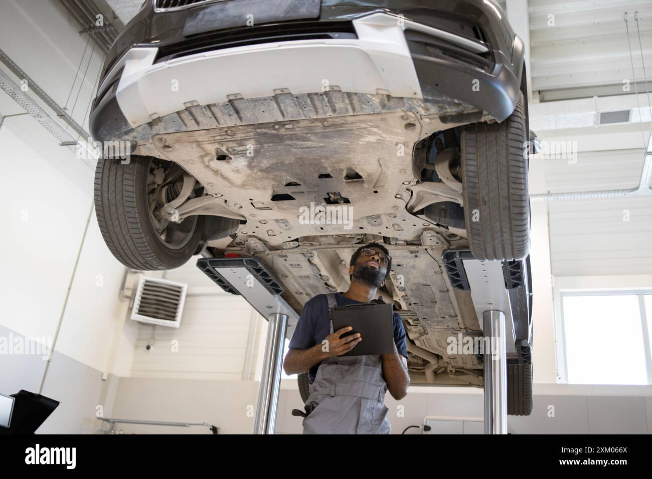 Mechanic inspecting car on lift in auto repair shop Stock Photo - Alamy