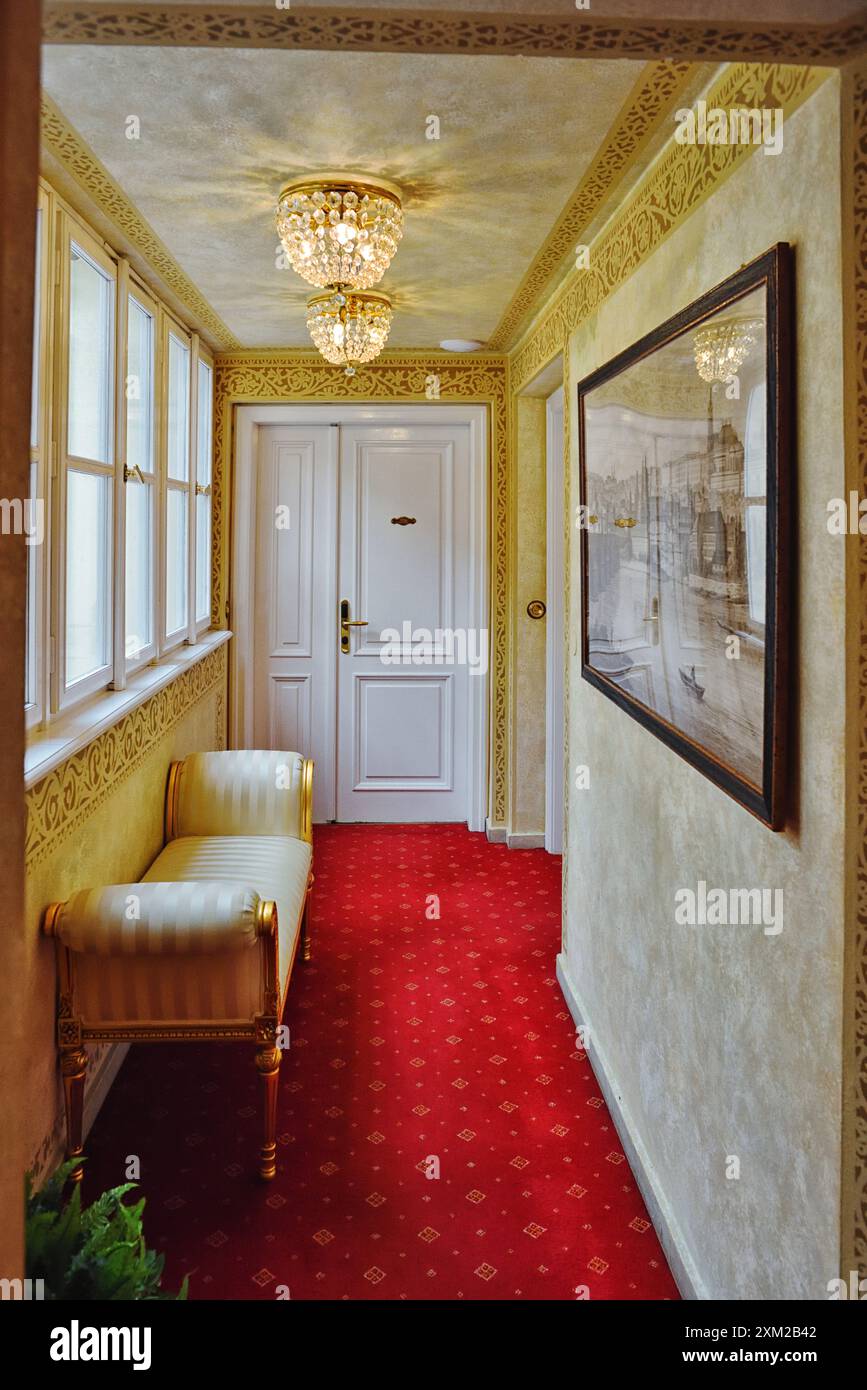 Hallway with a divan, ragged walls stenciled decorative details, red carpet two small chandeliers in a luxury hotel palazzo in Prague, Czech Republic Stock Photo