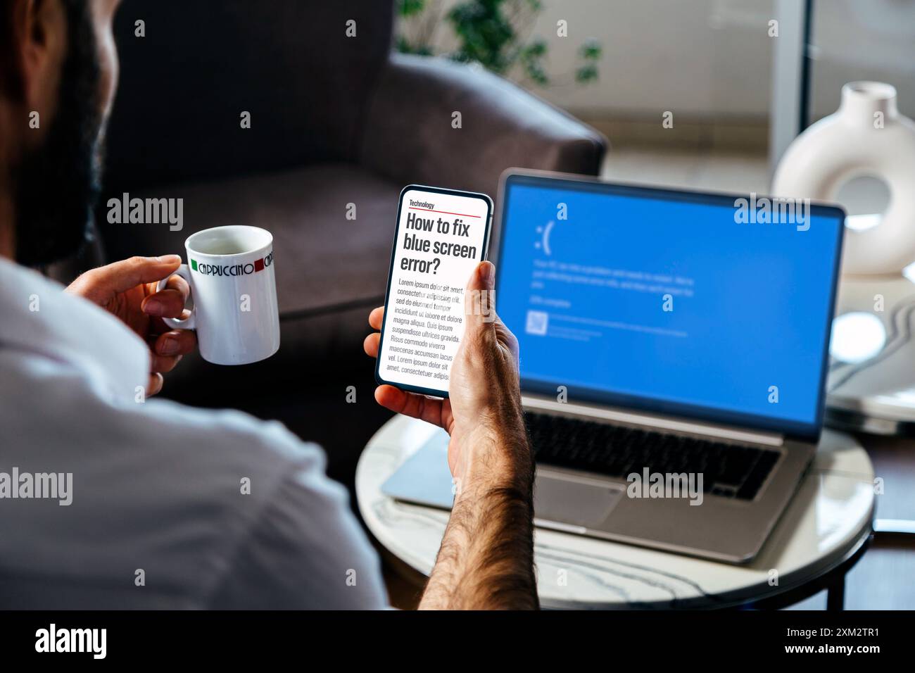 Man with mobile phone searching information to fix blue screen of death or BSOD of his laptop. Faulty operating system error. Stock Photo