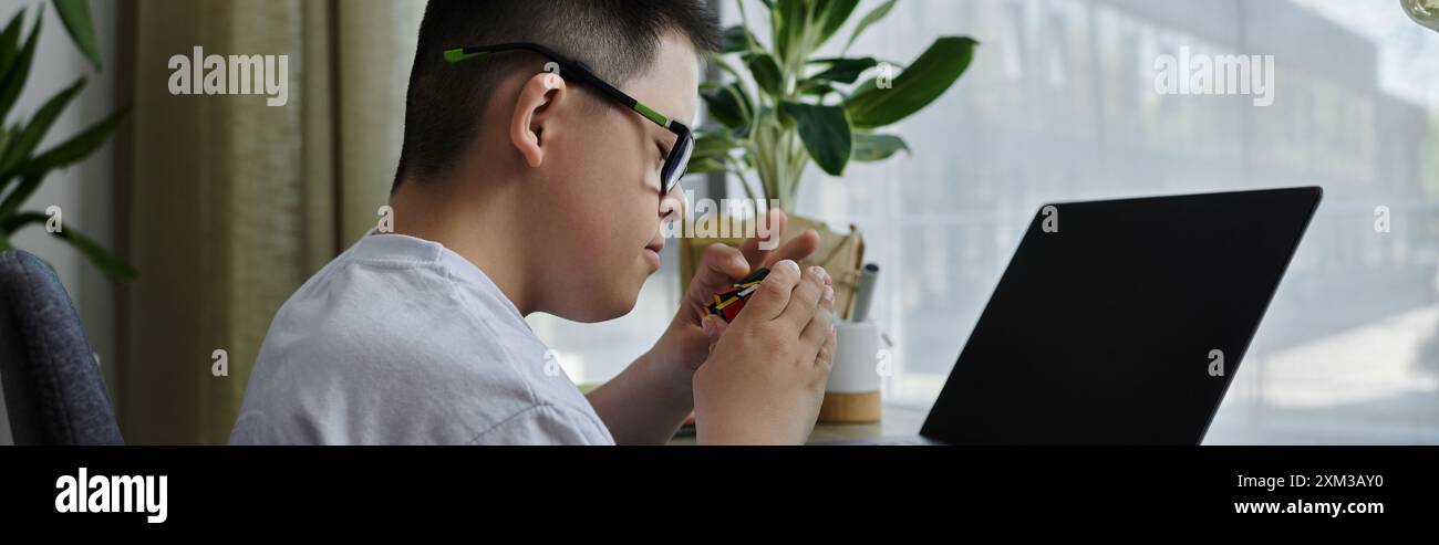 A young boy with Down syndrome sits at a desk in his home, intently working on a craft project. Stock Photo