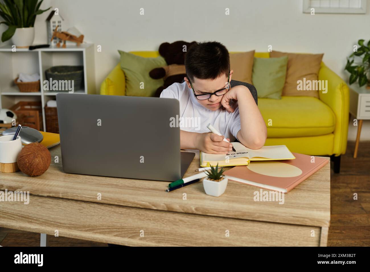 A young boy with Down syndrome sits at a table studying. Stock Photo