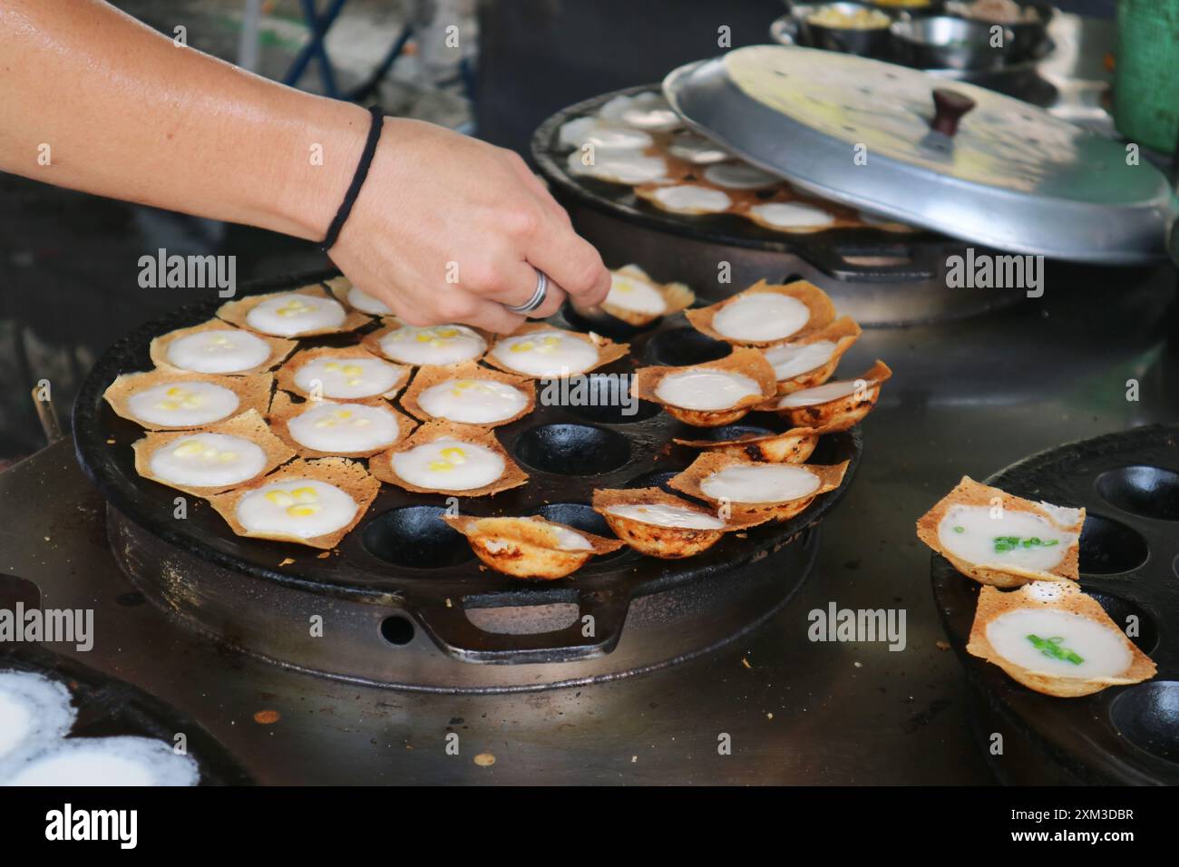 Vendor taking Kanom Krok, popular Thai coconut milk pancakes out from the pan when ready to serve Stock Photo