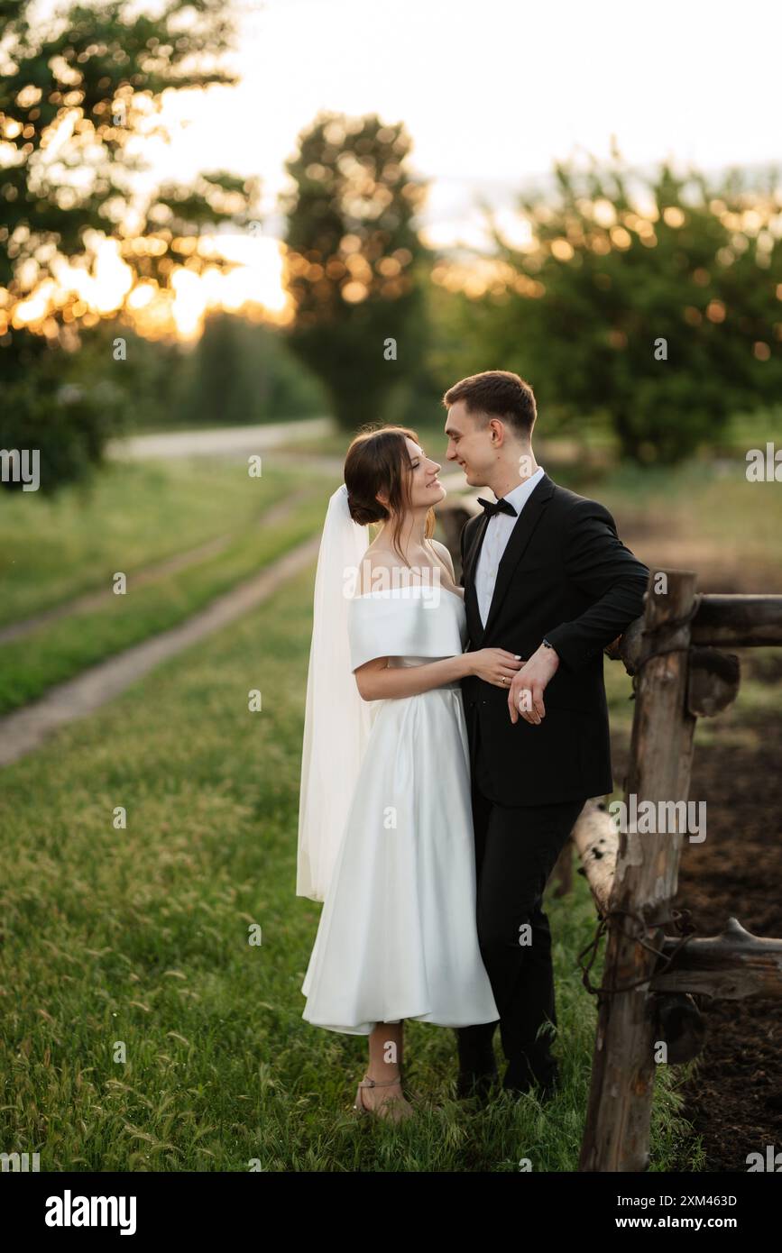 young couple the groom in a black suit and the bride in a white short dress on a walk in the village Stock Photo