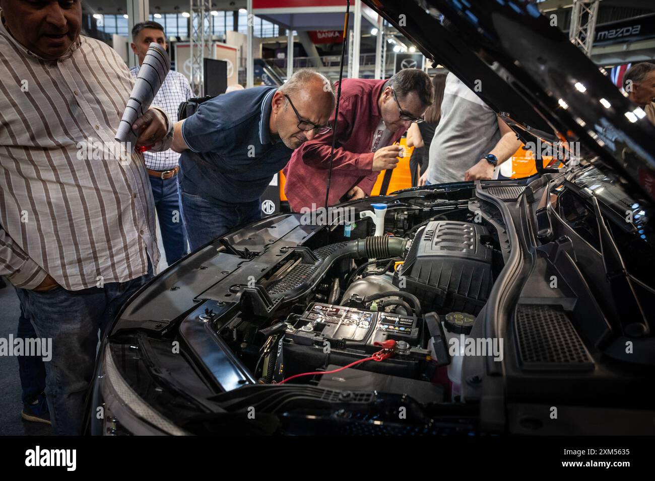 Potential buyers closely inspecting the engine of a brand new car at a ...