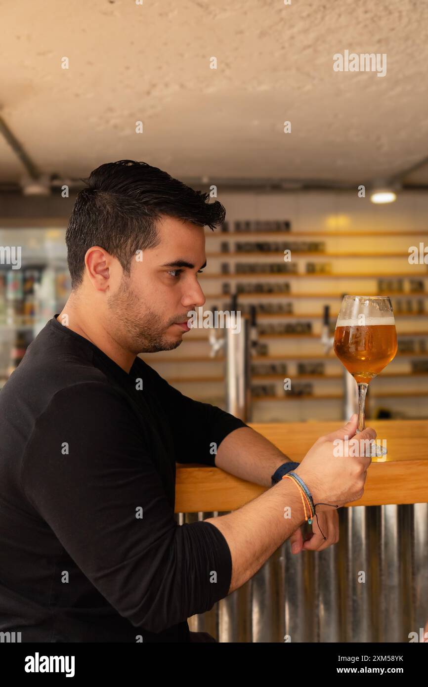 A Latin man in profile, looking appreciatively at his craft lager beer. Stock Photo