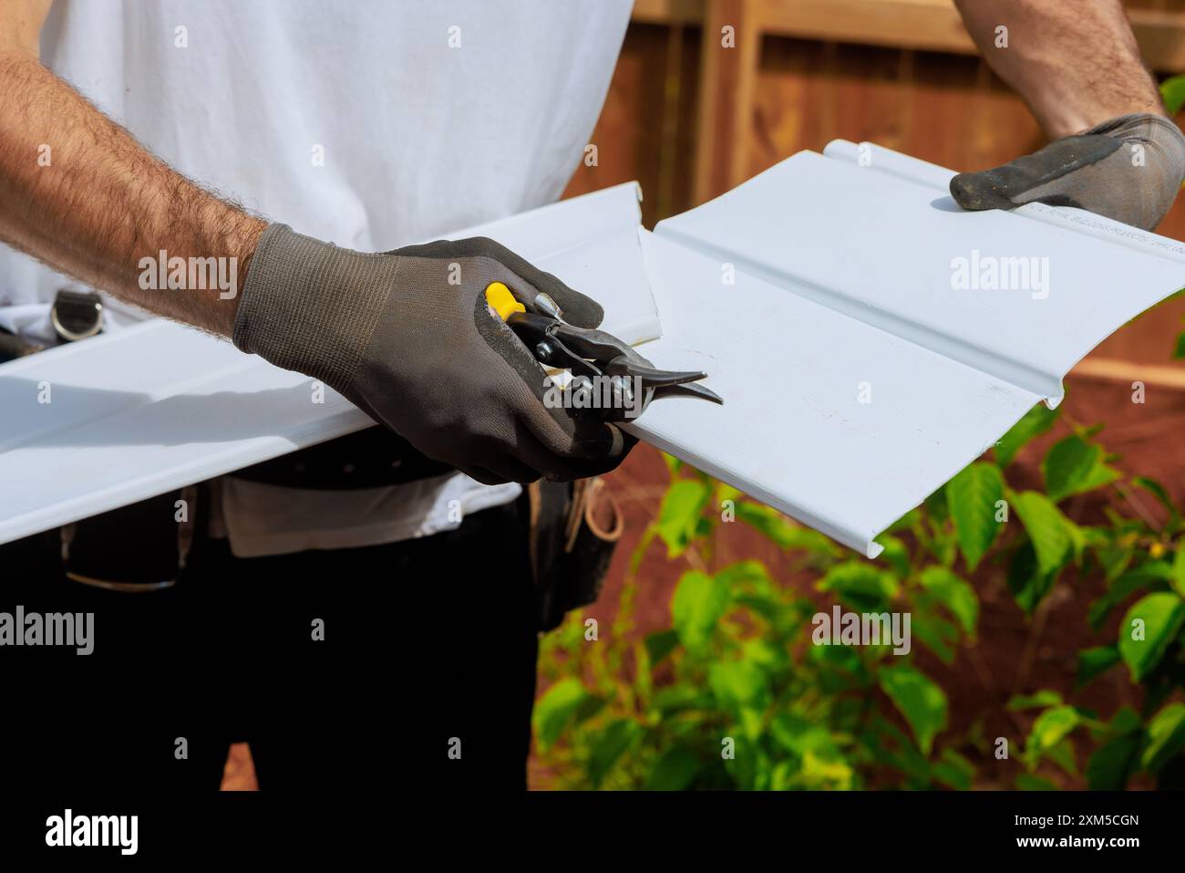 An individual cuts plastic vinyl siding to size before it is installed ...