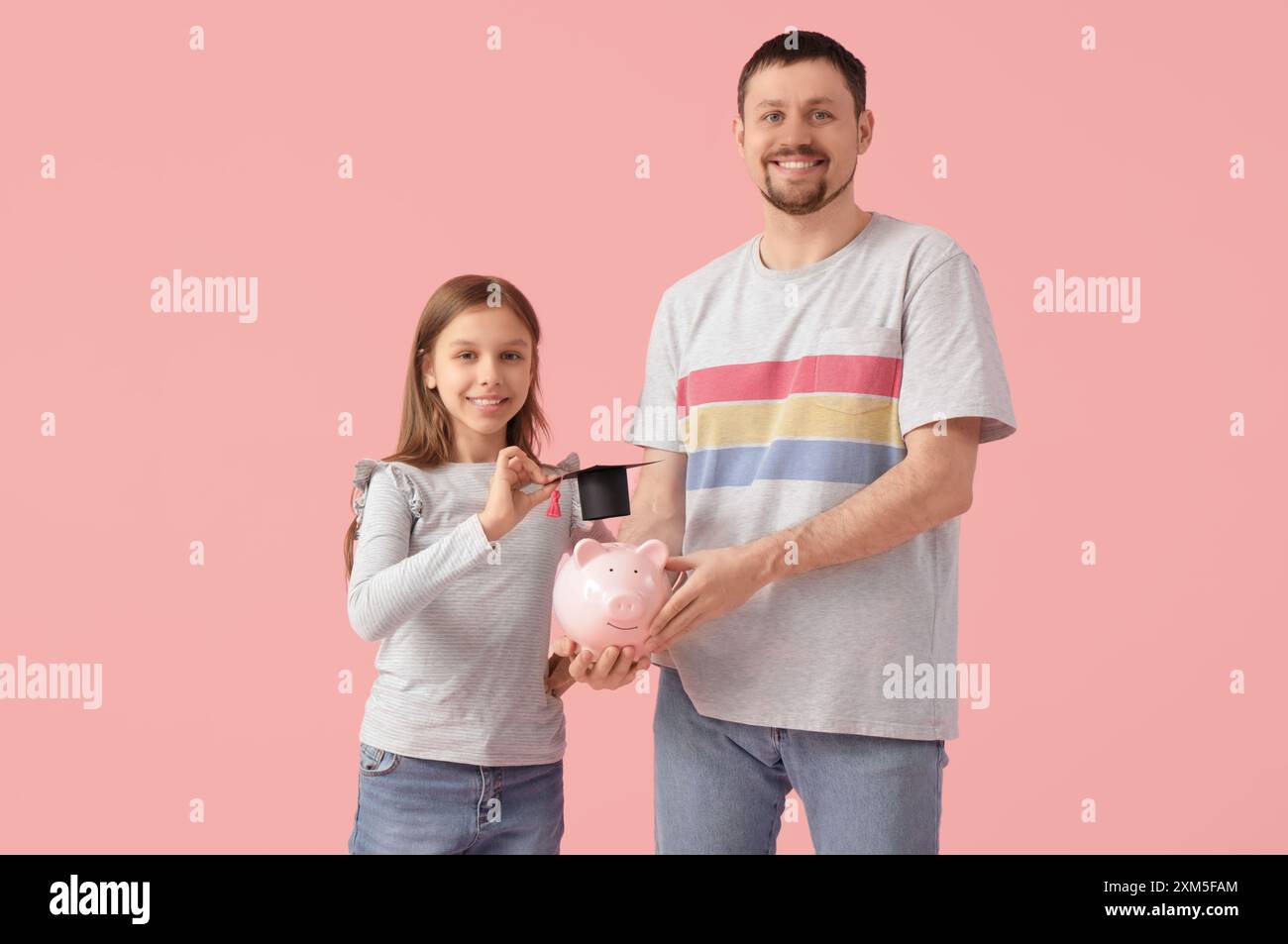 Father and his daughter holding piggy bank with mortar board on pink ...