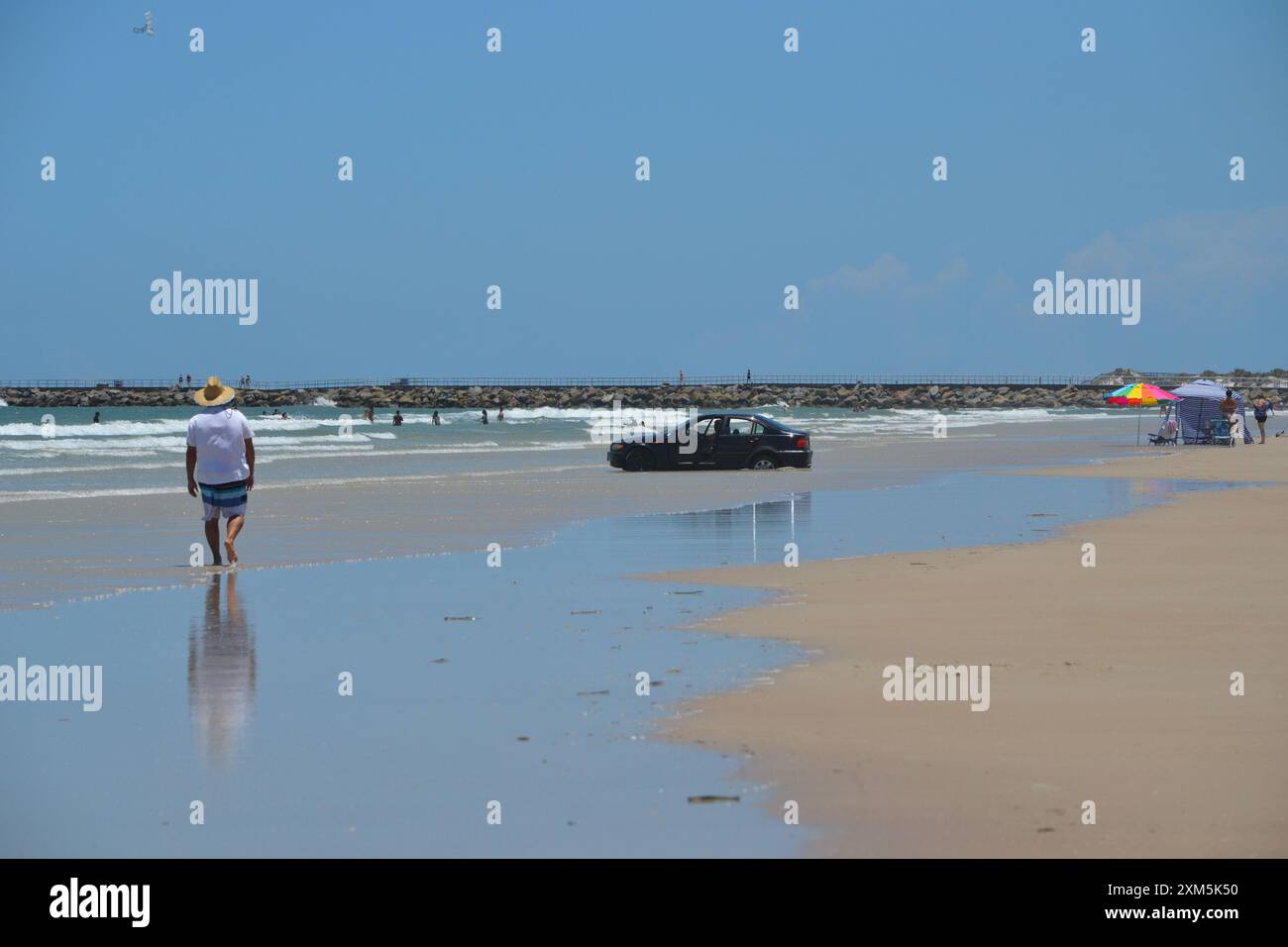 A beachgoer who parked his car at the ocean's edge found himself stuck as the waves rolled in, with onlookers watching the unfolding scene in Florida. Stock Photo