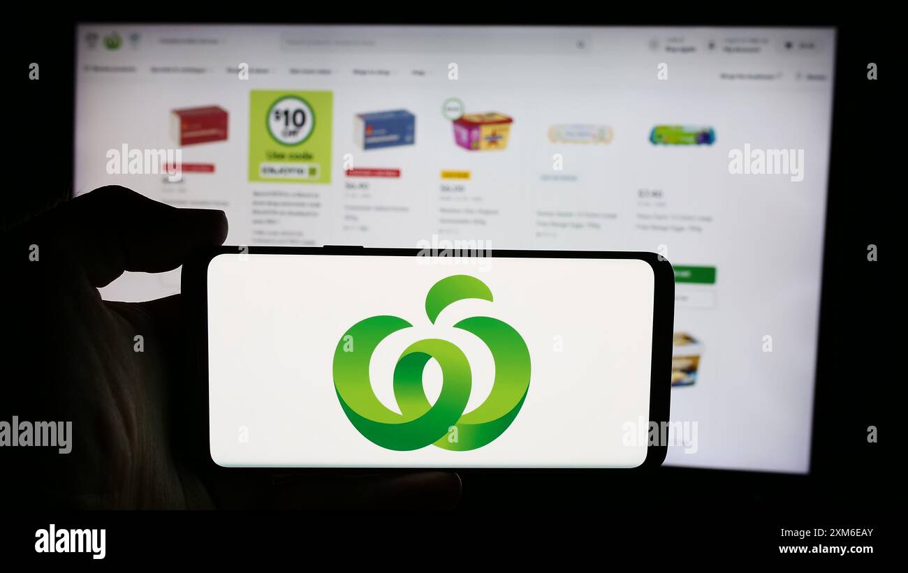 Person holding cellphone with logo of Australian retail chain company Woolworths Supermarkets in front of webpage. Focus on phone display. Stock Photo