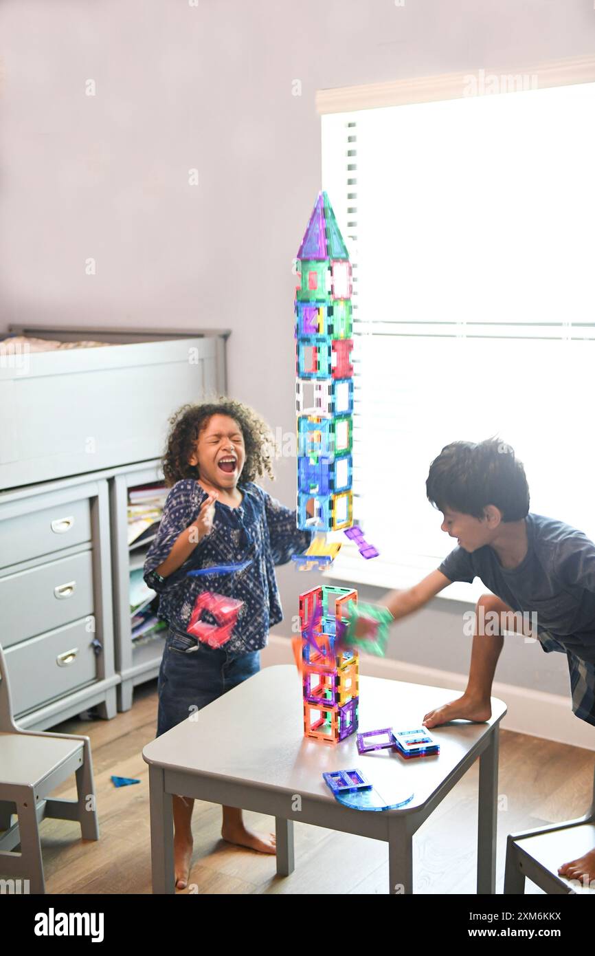 Two children joyfully knocking down colorful magnetic tiles, building a ...