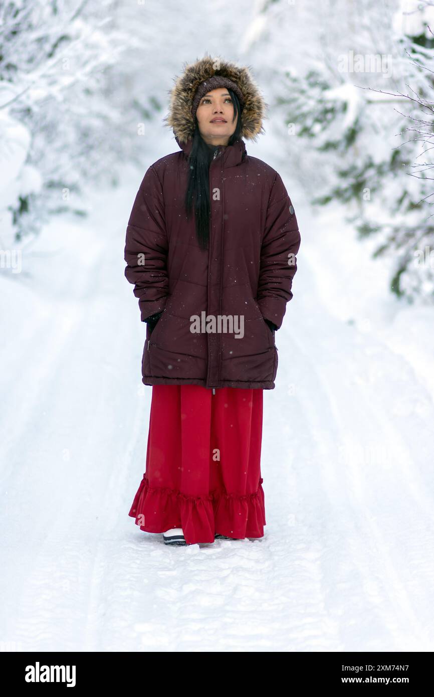 A young woman in a red suit and hooded jacket walks in a snowy forest Stock Photo