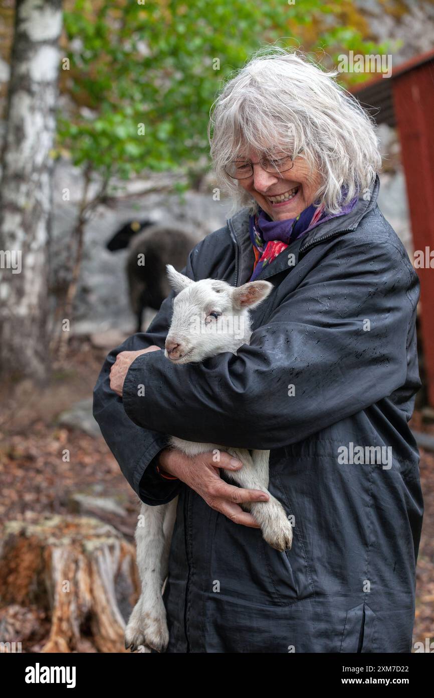 A middle-aged woman has a newborn lamb in her arms and smiles broadly, photo: Bo Arrhed Stock Photo