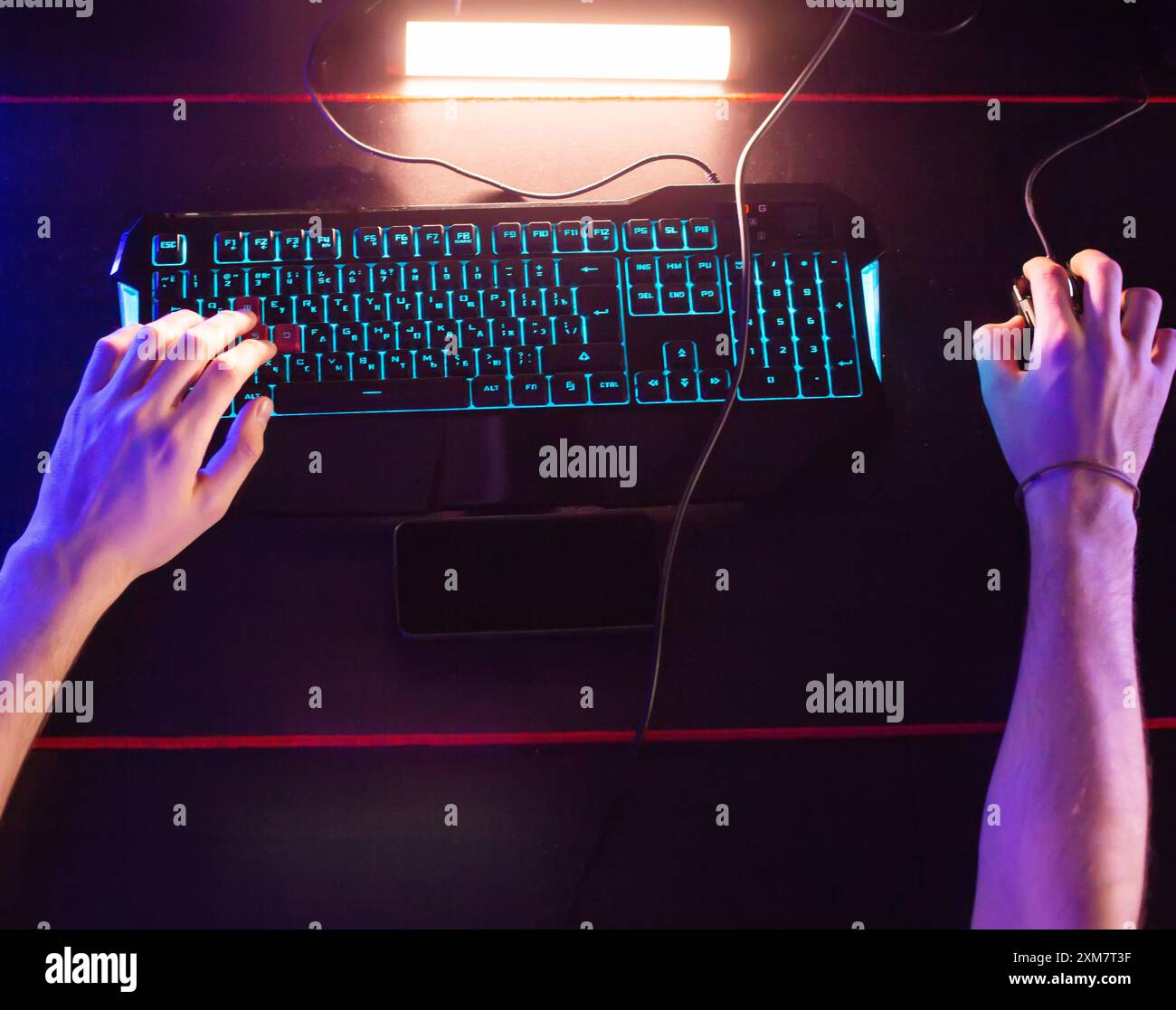 Gamer plays video game at computer club, fingers click on buttons of gaming mouse, keyboard with RGB lighting. Professional E-sport tournament, Cyber Stock Photo