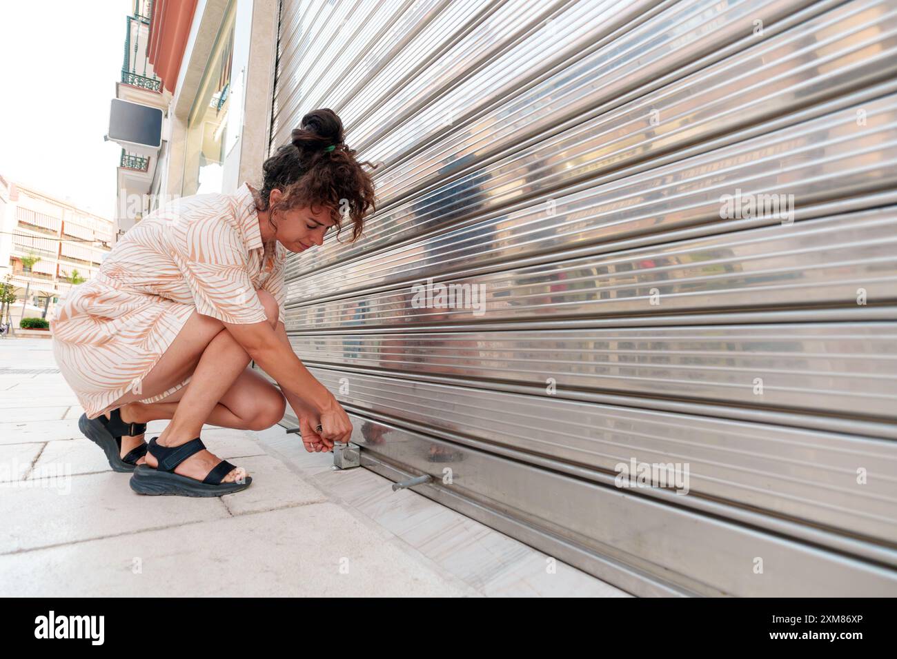 'Young woman unlocking a storefront shutter in the morning' Stock Photo