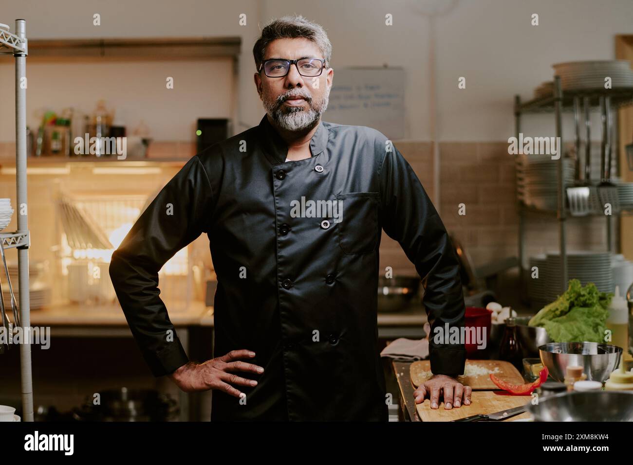 Highly experienced chef dressed in jet black uniform standing next to kitchen counter and looking directly at camera Stock Photo
