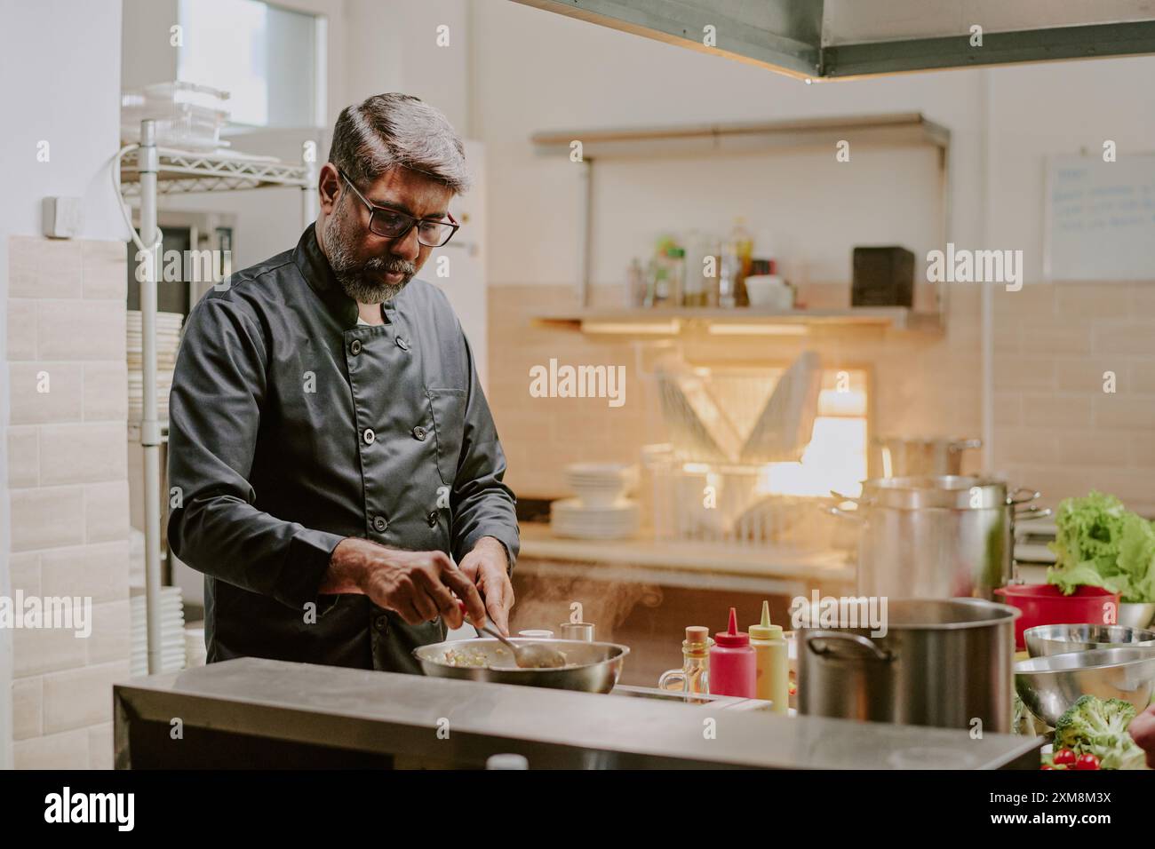 Highly skilled Indian chef frying special ingredients to add it into main course, at work in modern kitchen fully equipped with cookware Stock Photo
