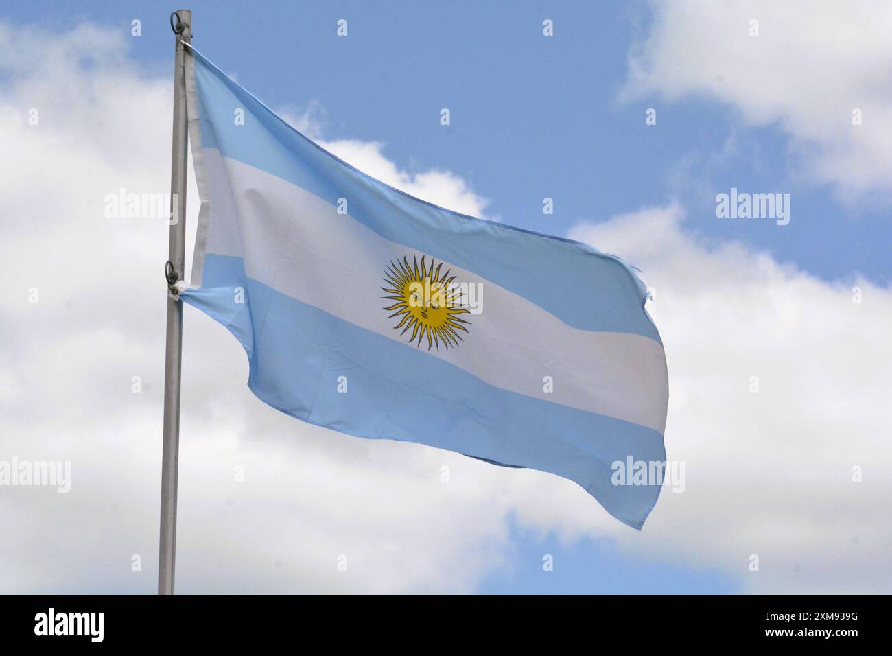 The national flag of the Argentine Republic flies up a flagpole on a beautiful summer day with a background of blue sky and white clouds. Stock Photo
