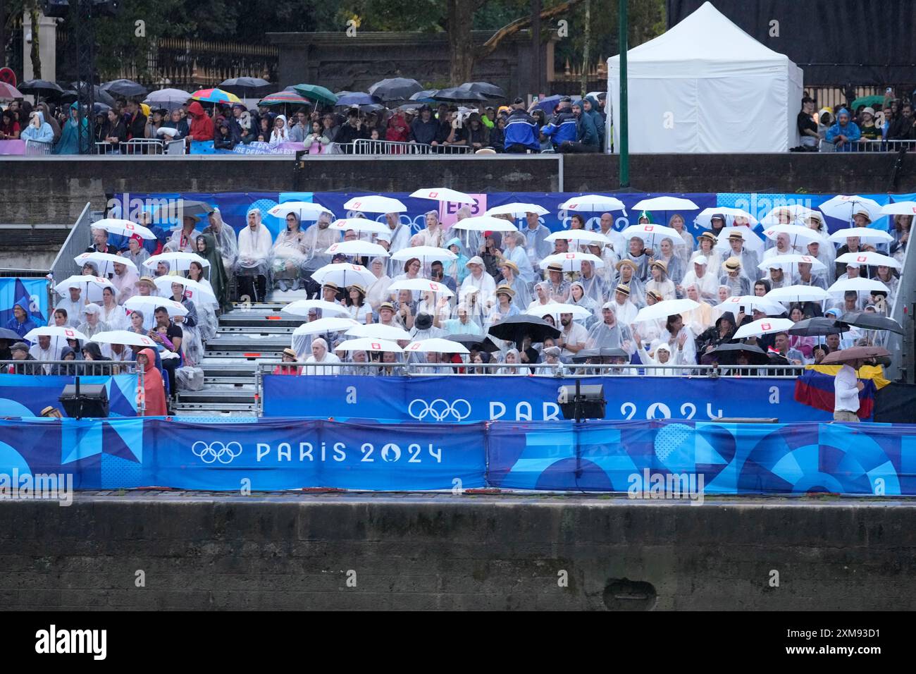 Spectators wear rain coats and holding umbrellas watch in Paris, France ...