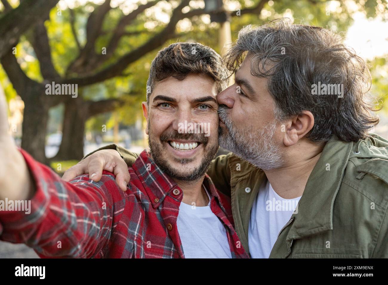 A happily married gay couple is smiling and kissing while taking selfies. Stock Photo