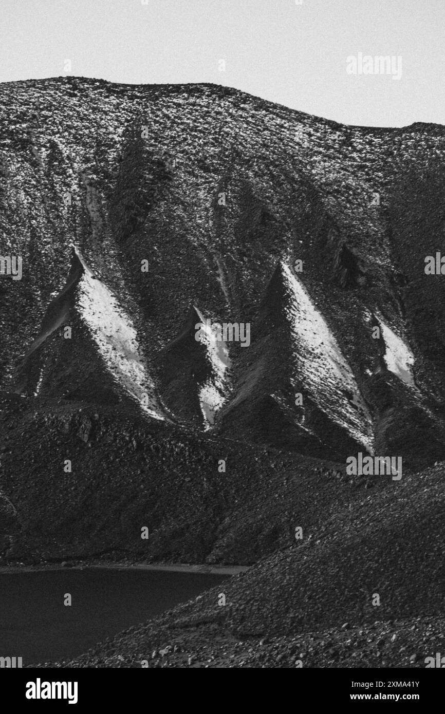 Black and white photograph showing snow-covered rocks and steep slopes of a barren mountain landscape, Tongariro National Park, New Zealand Stock Photo