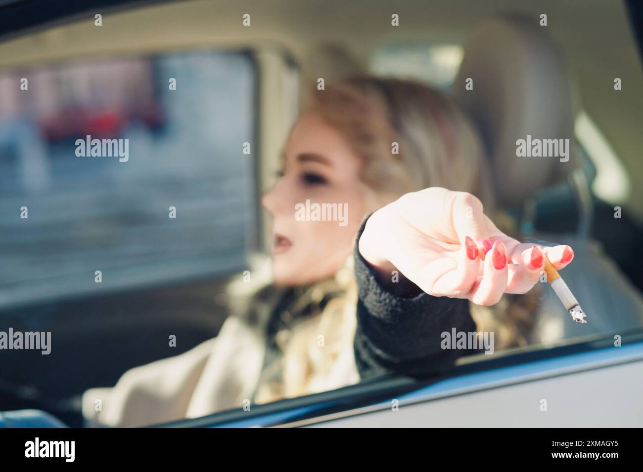 report someone throwing cigarette out window Young woman is throwing a cigarette butt out of the car window,  contributing to pollution and showcasing the issue of cigarette butt litter  Stock Photo
