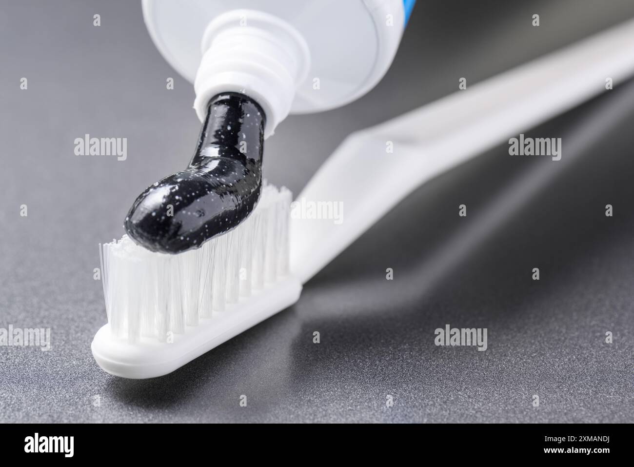 Black charcoal toothpaste being squeezed on white toothbrush Stock Photo