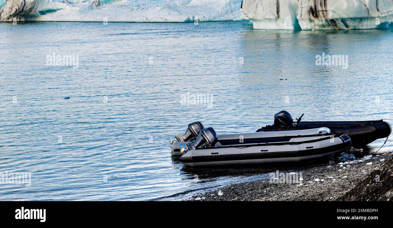 Two small boats are sitting on the shore of a lake full of icebergs ...