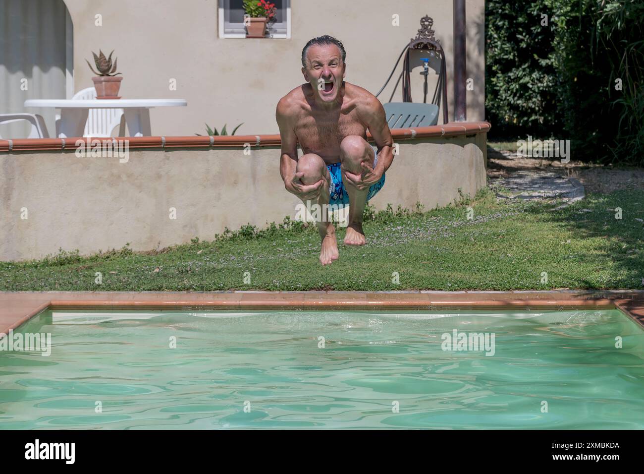 Middle aged man diving into a swimming pool, cannonball style,with a ...